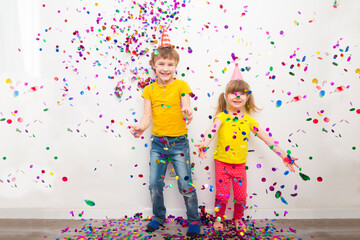 happy two kids  brother and sister with confetti on colored yellow background
