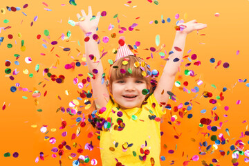 happy child girl with confetti on orange background. Holidays. Birthday
