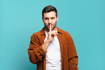 handsome adult blond man looking serious and cross with finger pressed to lips demanding silence or...