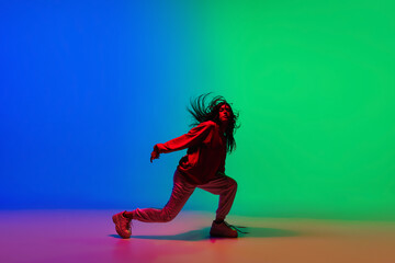 Fototapeta na wymiar Moving. Stylish sportive girl dancing hip-hop in stylish clothes on colorful background at dance hall in neon light. Youth culture, movement, style and fashion, action. Fashionable bright portrait.
