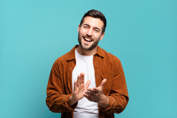 handsome adult blond man feeling happy and successful, smiling and clapping hands, saying...