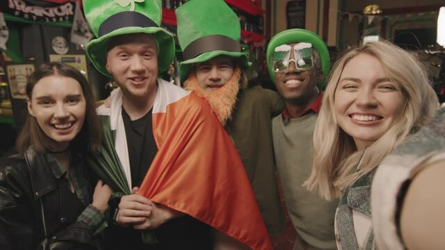 Handheld POV close up with slowmo of cheerful multi-ethnic group of friends in green hats having fun together on St Patricks Day celebrating in Irish pub
