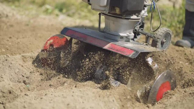Tiller - motor cultivator working on garden, cultivating soil for new season. Farmer in light roba and rubber boots cultivates the soil. Footage Full HD. Very close view