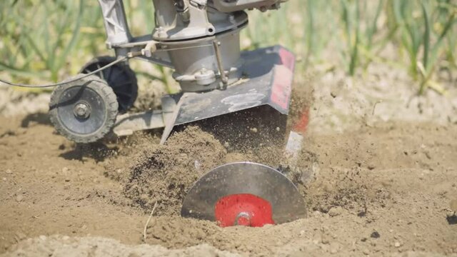 Tiller - motor cultivator working on garden, cultivating soil for new season. Farmer in light roba and rubber boots cultivates the soil. Footage Full HD. Very close view