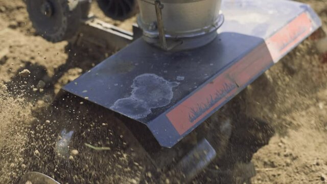 Tiller - motor cultivator working on garden, cultivating soil for new season. Farmer in light roba and rubber boots cultivates the soil. Footage Full HD. Very close view