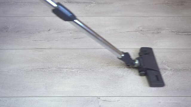 The vacuum cleaner's brush sucks in dust on the gray laminated surface. Apartment cleaning, vacuuming gray parquet and laminate flooring, weekly general cleaning of the maid