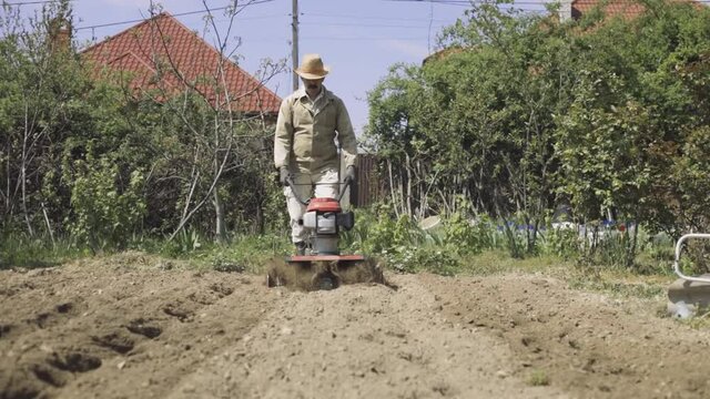  Tiller - motor cultivator working on garden, cultivating soil for new season. Farmer in light roba cultivates the soil. Footage Full HD. Very close view