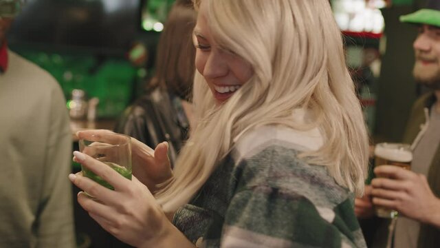 Medium closeup with slowmo of pretty young blonde woman looking at camera dancing to music in Irish pub with company of multiethnic friends celebrating St Patricks Day