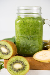 Vegan green smoothie in a jar with spinach, banana and kiwi on a white background