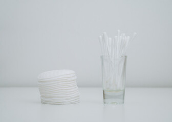 Fototapeta na wymiar Close-up of stack of cotton pads and cotton swabs in a glass cup. White background.