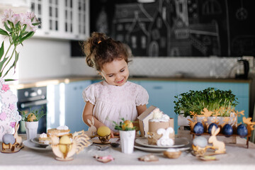 Little cute girl paints Easter eggs at home in the kitchen with a brush. Happy childhood. Festive creativity. Christian light kind tradition. The child is a Christian. Oriental appearance. Life style 