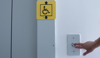 female hand presses the button to call the elevator inside, yellow sign of the possibility of using the elevator for people with disabilities, calling the elevator in a residential building