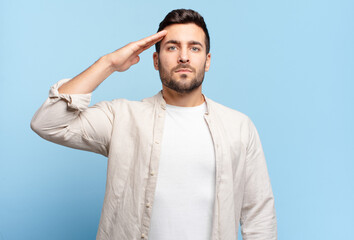 handsome adult blond man greeting the camera with a military salute in an act of honor and...
