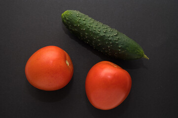 Three red tmatoes and green cucumber on black background. Top view. Healthy  fresh vegeterian food.