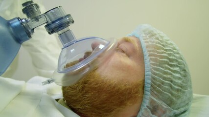 Close up tracking shot of male patient lying on gurney with eyes closed and receiving bag-valve-mask ventilation while being transported to emergency room