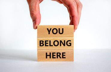 You belong here symbol. Wooden blocks with words 'You belong here' on beautiful white background. Businessman hand. Diversity, business, inclusion and belonging concept.