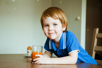 Cheerful child drinks juice for Breakfast in the kitchen.