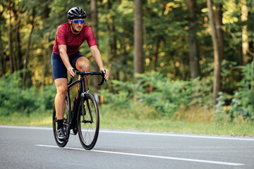 Muscular guy in helmet riding bike on asphalt road