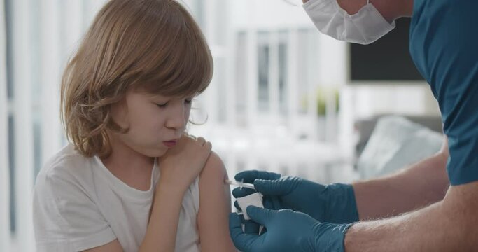 Close up of aged doctor in protective mask and gloves vaccinating preteen boy