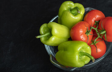 Fresh ripe peppers and tomatoes in glass bowl over black background