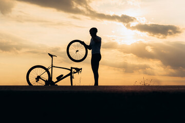 Silhouette of strong man fixing wheel on bike outdoors