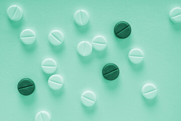 Green tinted background on the theme of medicine, health care, drugs, pharmacology. Light tablets and dark pills lie on paper sheet. Pharmacological backdrop close-up. Top view from above. Macro