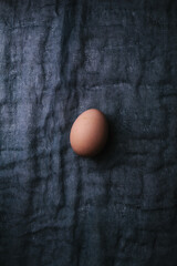 One egg on dark fabric background. Easter, spring or eco food concept. Top View