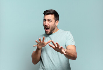 young handsome adult man feeling terrified, backing off and screaming in horror and panic, reacting...