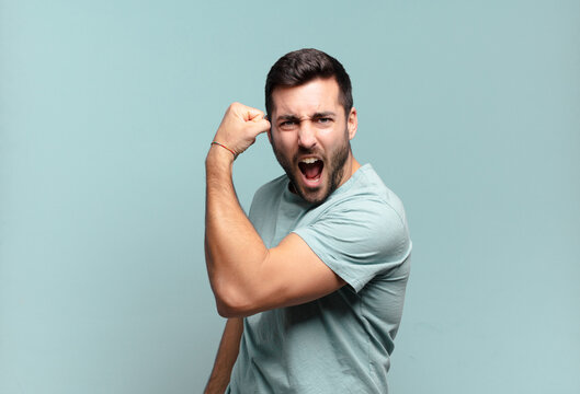 Young Handsome Adult Man Feeling Happy, Satisfied And Powerful, Flexing Fit And Muscular Biceps, Looking Strong After The Gym