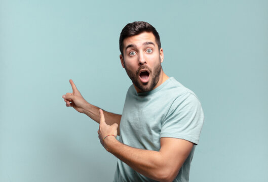 young handsome adult man feeling shocked and surprised, pointing to copy space on the side with amazed, open-mouthed look