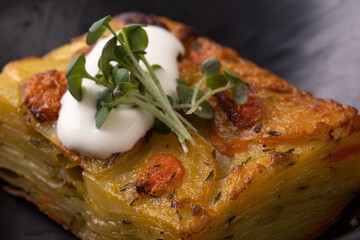 Potato gratin with sour cream and micro greens in black plate shot from the top