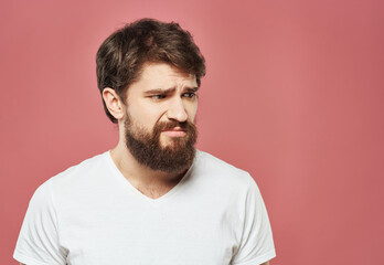 Fototapeta premium Portrait of an upset man in a white t-shirt on a pink background cropped view
