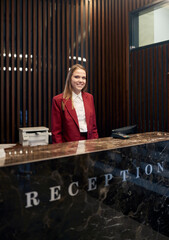 A pleasant female receptionist waiting for the guests behind the counter. Tourism, business, hotel