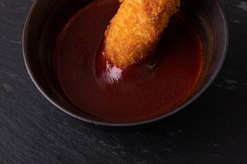 Crispy golden fish finger getting dipped in a bowl of sauce