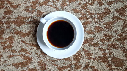 Top view of white cup of black coffee on brown rug or carpet background with copy space. Flat lay of hot drinking on cotton floor wallpaper.