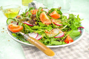 Fresh colorful spring salad with tomatoes, avocado, walnuts, cucumber, spring radish, on light green background copy space. Spring diet healthy food concept