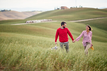 A young cheerful couple feeling happy while walking a large meadow together. Love, relationship, together, nature
