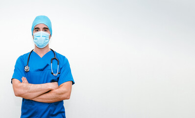 Doctor in surgical outfit and mask standing with his arms crossed