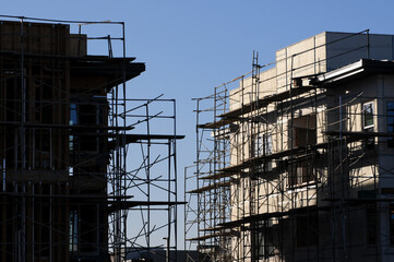 Framed and stuccoed multi-story buildings under construction with surrounding scaffolding, illustrating stages of multi-family residential development in urban infill projects