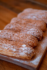 several long chocolate eclairs with white sprinkles on a wooden board, close, with a blur