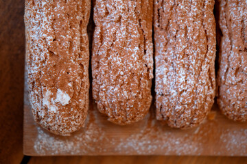 several long chocolate eclairs with white sprinkles on a wooden board, close, with a blur