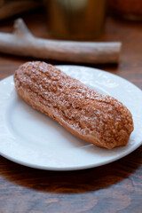 long chocolate eclair with sprinkles on a white plate, close, with a blur