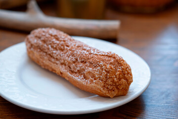 Long chocolate eclair with sprinkles on a white plate, close, with a blur
