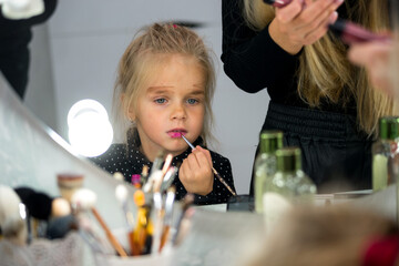 portrait of a blonde girl in the reflection of the mirror. daughter imitates mom and does makeup on her own