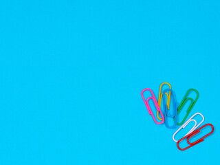 Collection of colorful paper clips on blue background with copyspace