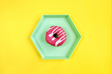 Tasty pink glazed doughnut on green hexagon plate on yellow background. Top view of delicious...