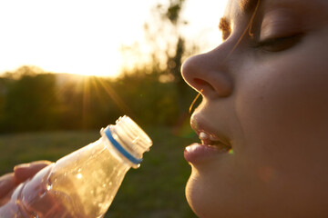 woman drinks water from a plastic bottle in summer outdoors