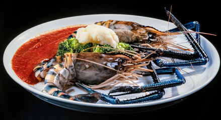 Cooked Spiny Lobsters with blue claws on the white plate isolated on black background