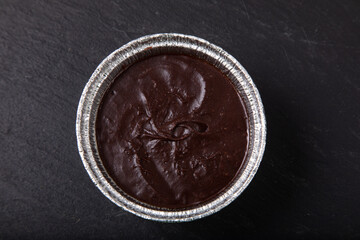 Melted milk chocolate in foil pot on dark brown table