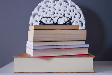 group of reading books resting on a table with black reading glasses on a grey background and a...